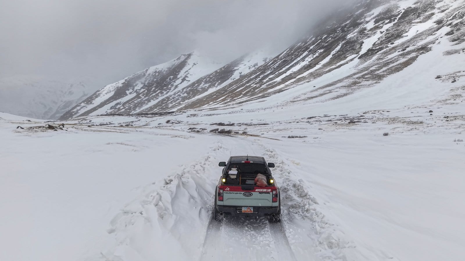 Ford Ranger Raptor with Adventure Lab gear navigating deep snow on mountain road with storm clouds overhead
