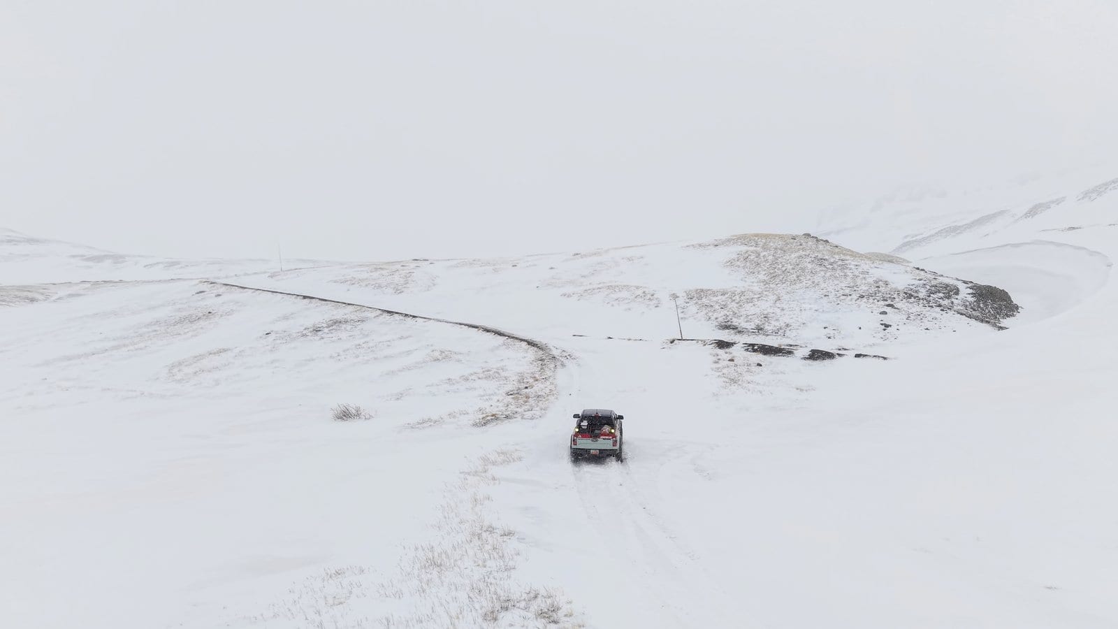 Off-road truck crossing vast snow-covered alpine terrain with rolling hills and power lines visible