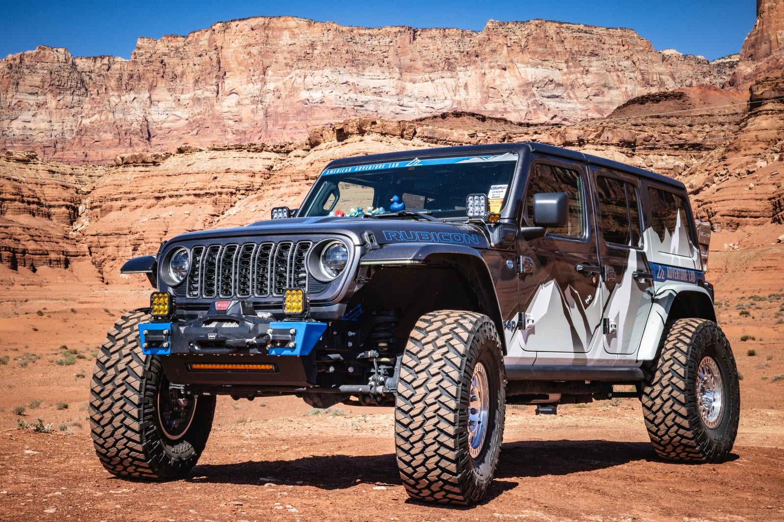 Side profile of the Sparky Wrangler Rubicon 4xe beside Marble Canyon's desert landscape.