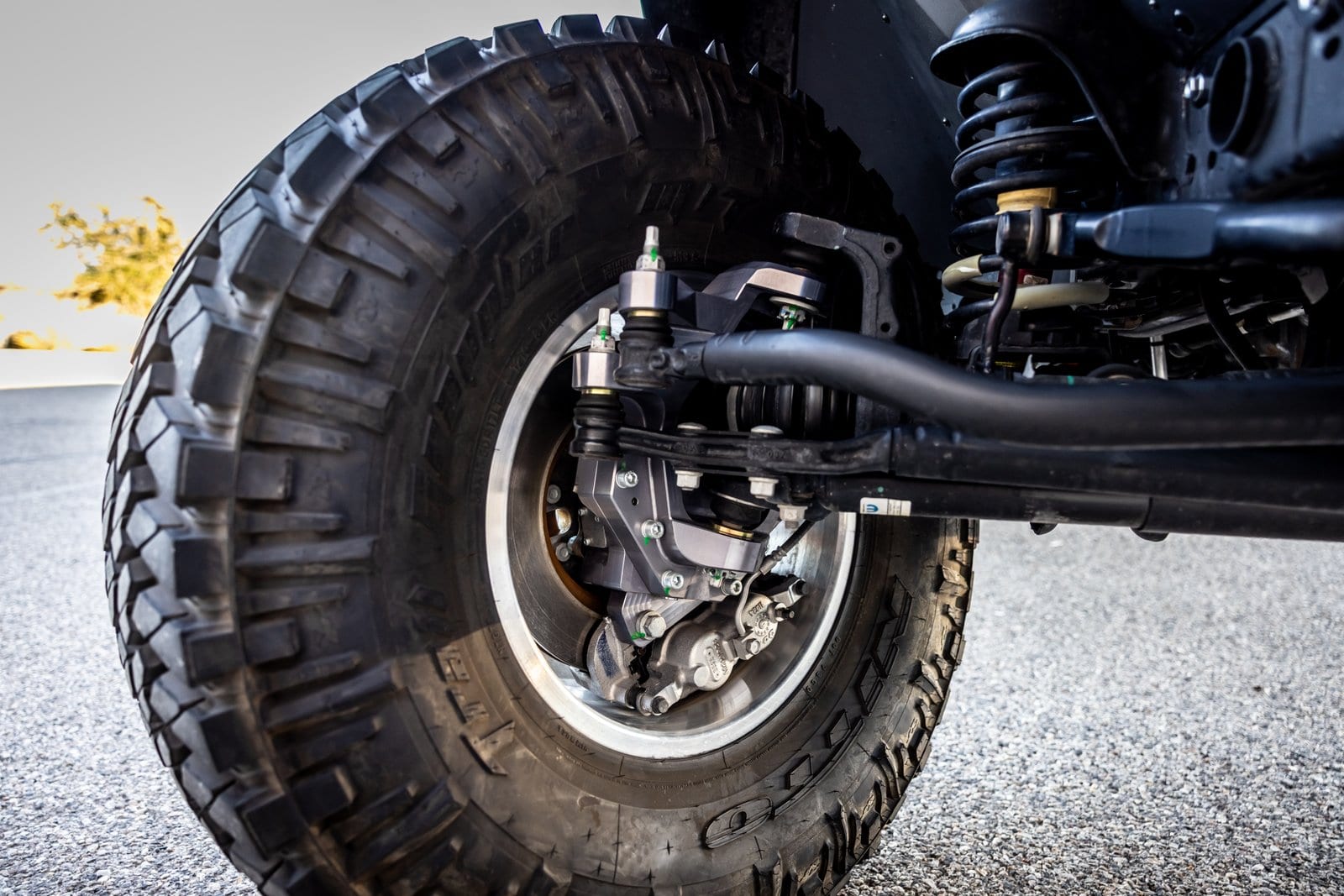 Close-up of an off-road rear wheel, tire, and suspension setup with coil spring and control arms.