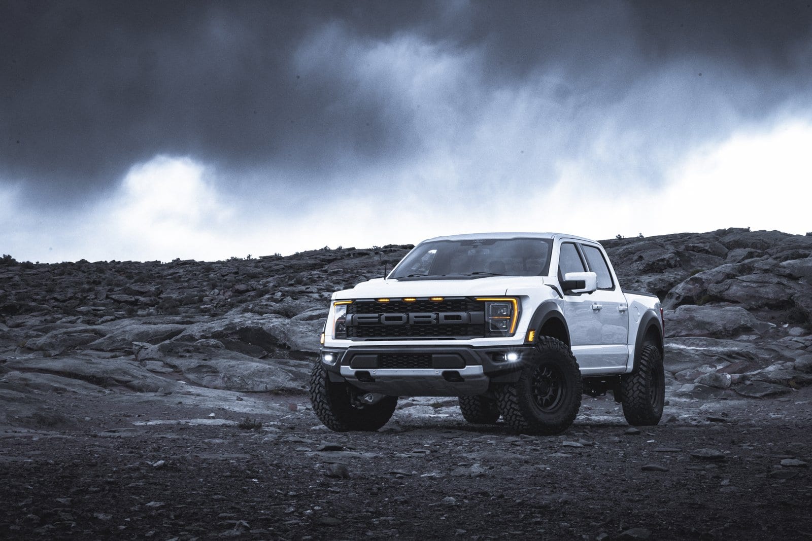 White Ford F-150 Raptor parked on rocky desert ground with amber lights on