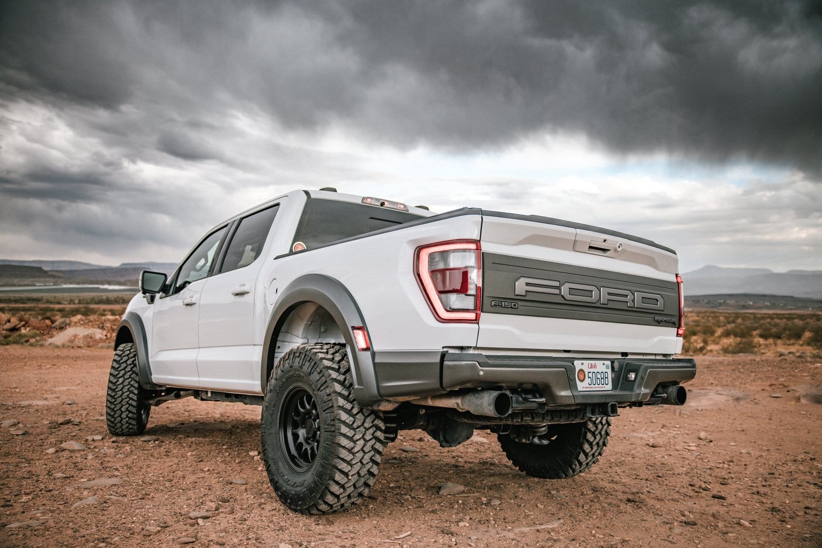 Rear three-quarter view of a white Ford F-150 Raptor on a desert plain