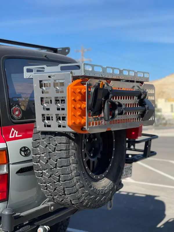 Raw aluminum STP Mini mounted above a Toyota spare tire with orange traction boards and tools