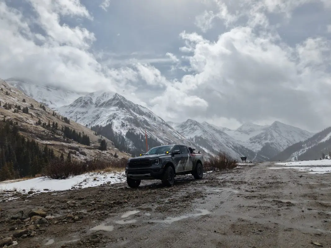 Off-road truck on a muddy San Juan mountain road with snow-covered peaks in the background