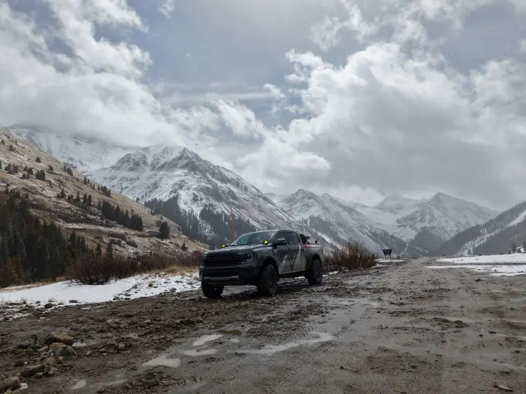 Off-road truck on a muddy San Juan mountain road with snow-covered peaks in the background