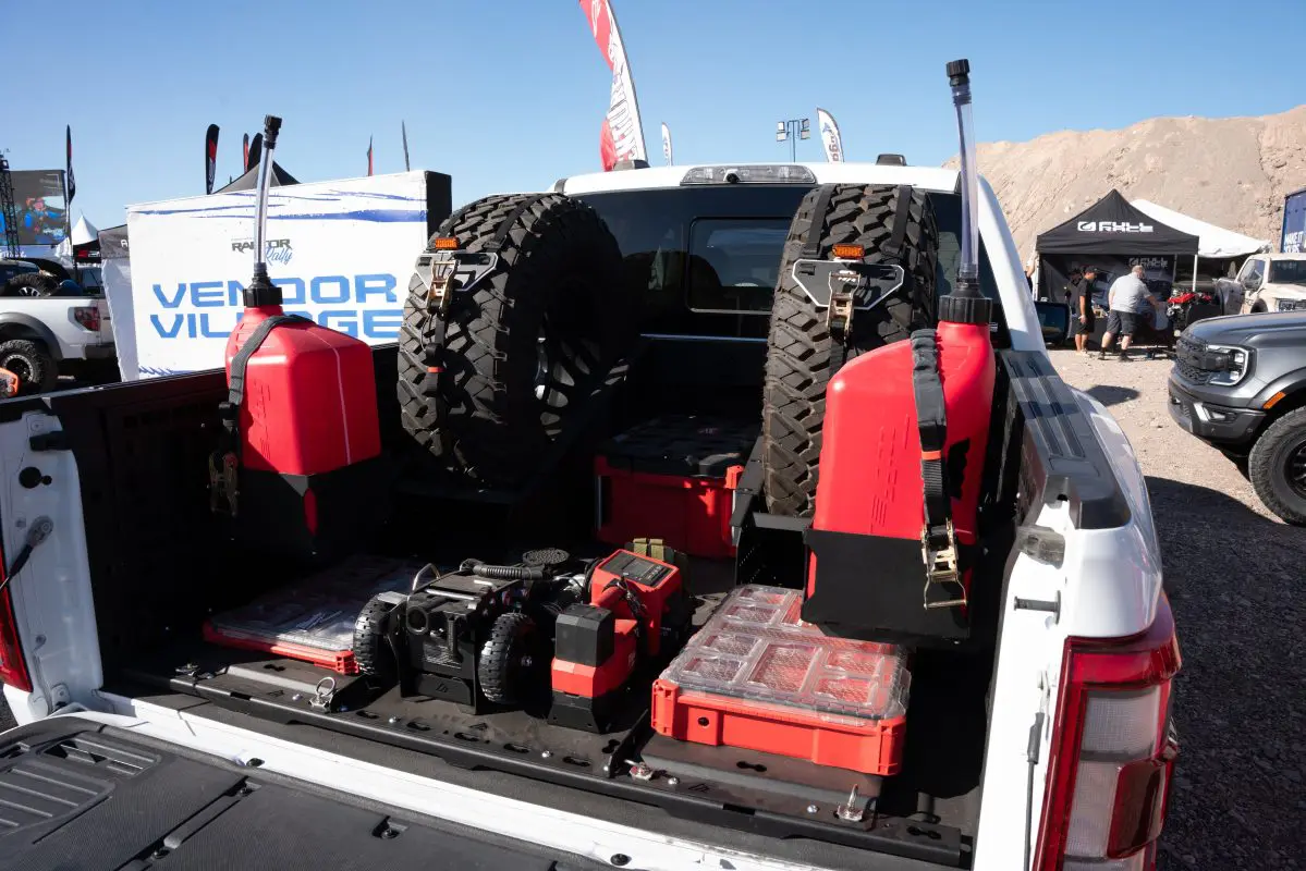 Angled view of an F-150 BASE bed layout with rear PACKOUT cases, upright spare tires and center-mounted equipment
